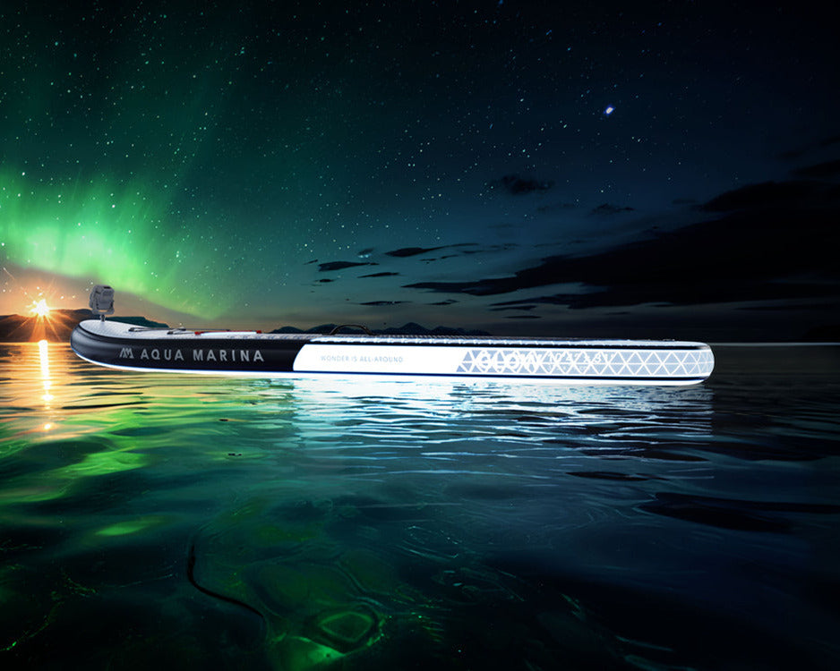 A long, slim white LED light bar labeled 'AQUA BREEZE' floating on dark water at night under a starry sky with green aurora borealis. Large text on the left reads 'GLOW INTO THE NIGHT'.
